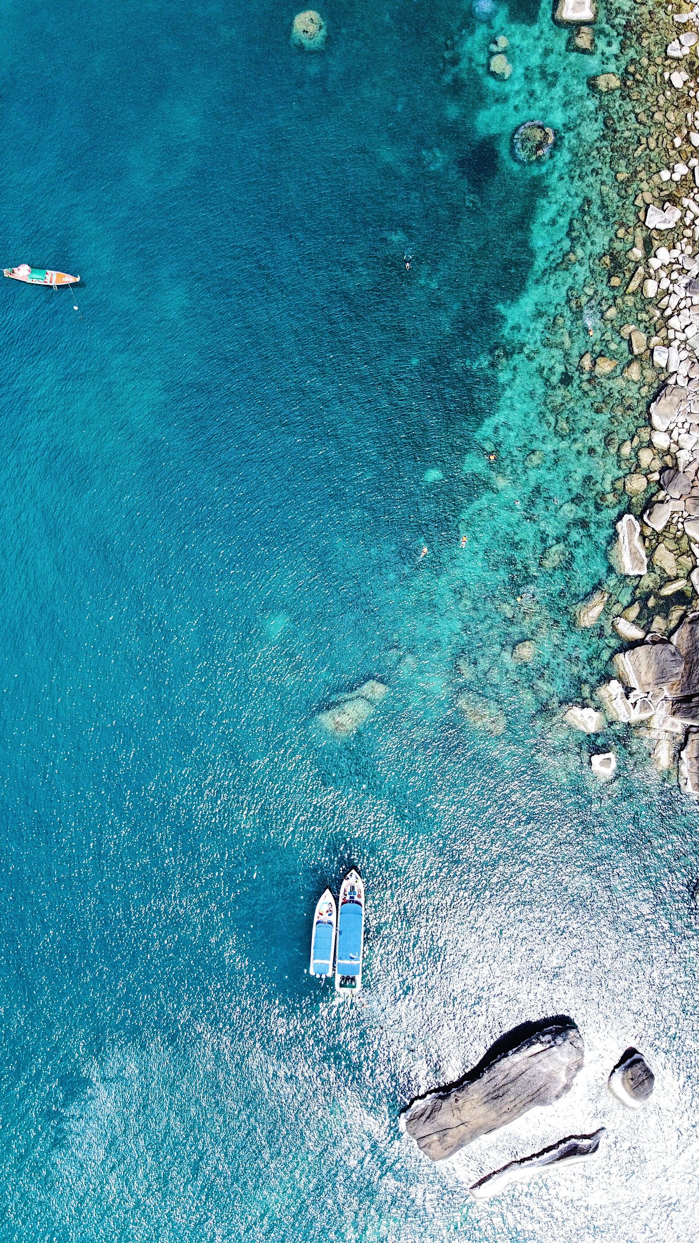 Boats in turquoise water beside the rocky coast of Koh Samui